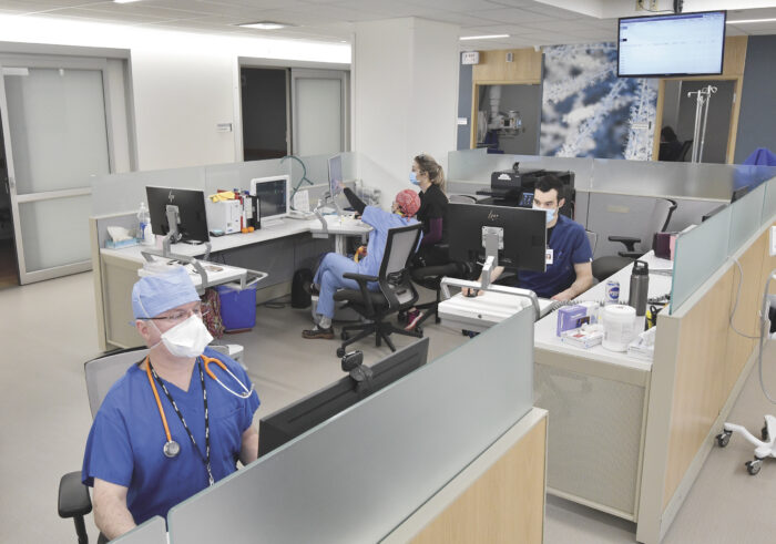 Emergency Room Physicians at Minnesota Hospitals are diligently working in a bustling clinic setting. Clad in scrubs and masks, they navigate through an array of medical equipment and screens, embodying the commitment to healthcare excellence that EPPA Health champions.